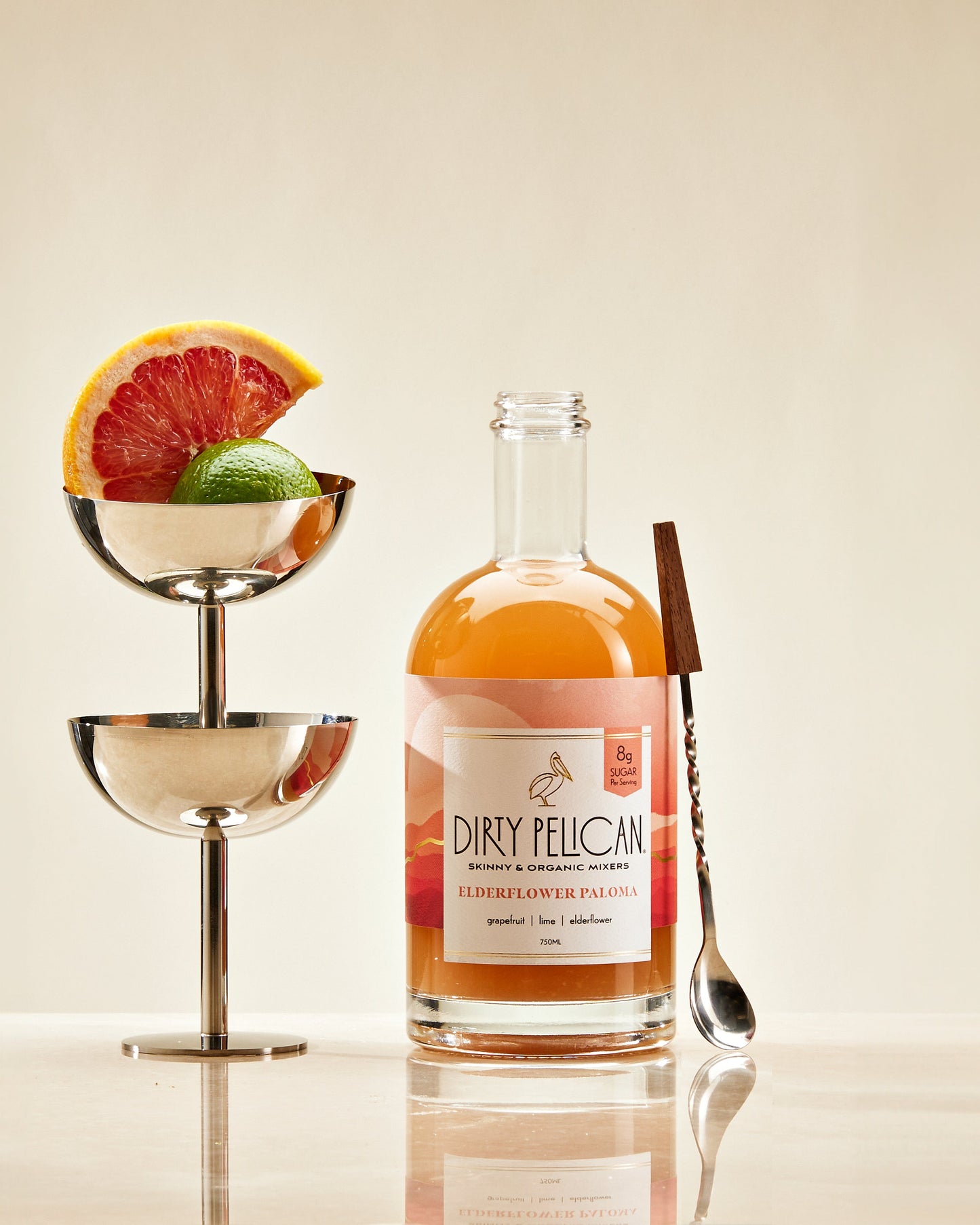 Bottle of Dirty Pelican elderflower paloma with cocktail garnishes on a reflective surface.