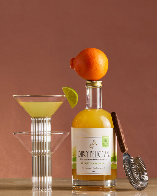 Bottle of Dirty Pelican cocktail with a cocktail glass and bar tools on a brown background